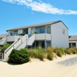 A beautiful two story condo and the view of it's backyard along a sandy beach. The house is white with a brown roof, white stairs that lead to the sand have bushes along the home. Some are regular bushes others are tall bushes with grass like foliage. This image is used as a visual aid regarding using a mortgage for brrrr