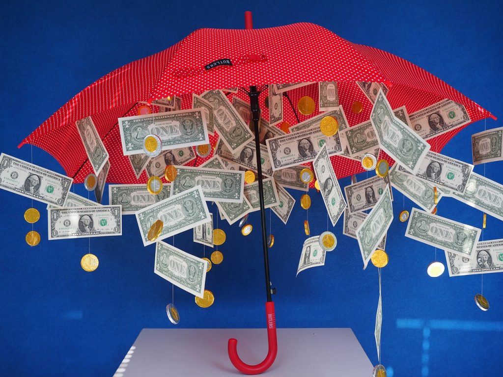 a red umbrella is being held up against a royal blue background with bills and coins hanging from the inside of the umbrella. the umbrella appears to stand on it's on on top of a white table. this visual aid to regarding the need to be rich to invest in real estate